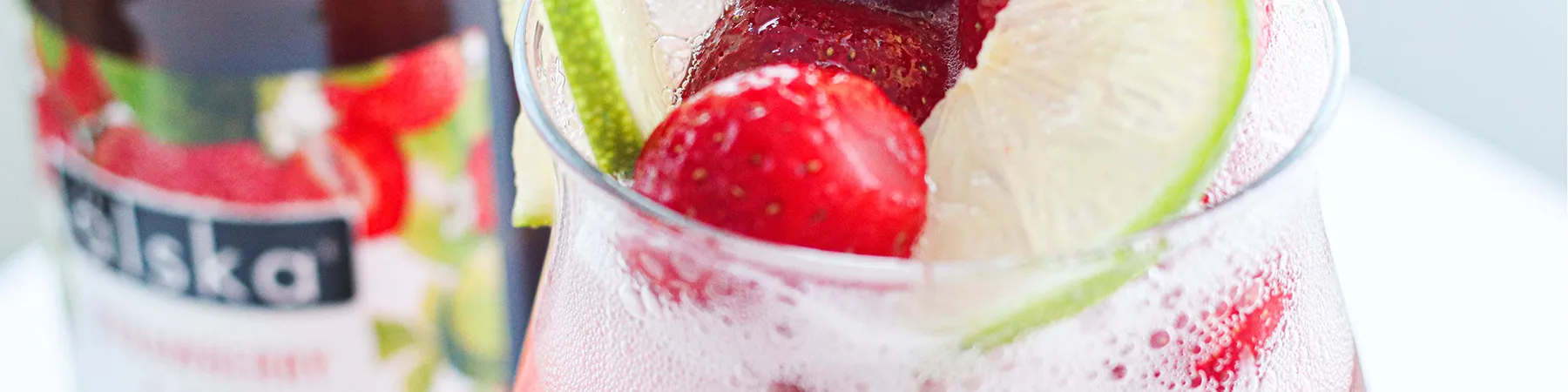 close up of glass of alska cider with ice and fruit in and bottle in background