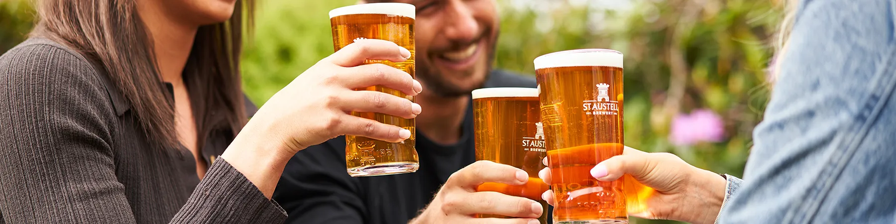 three people holding pints of st Austell beers outdoors