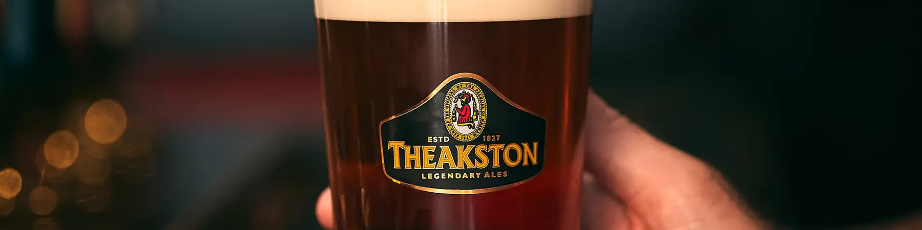 man holding close up of pint glass with Theakston beer