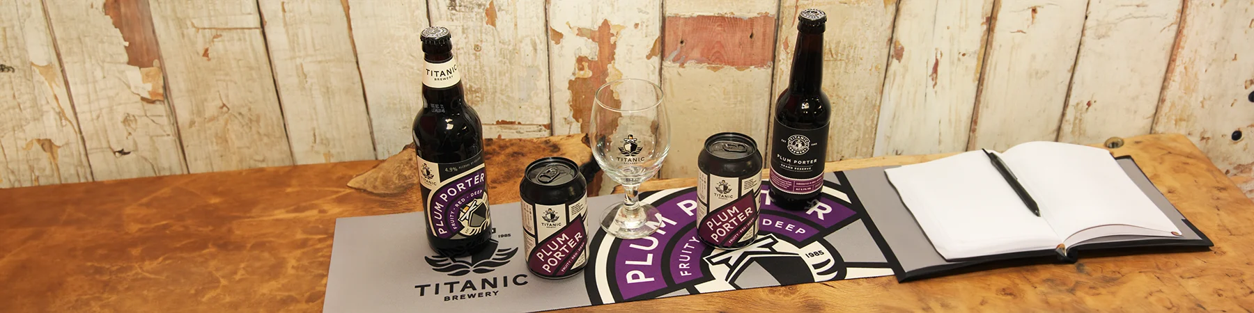 bottles and cans of titanic plum porter beers on logo runner next to book