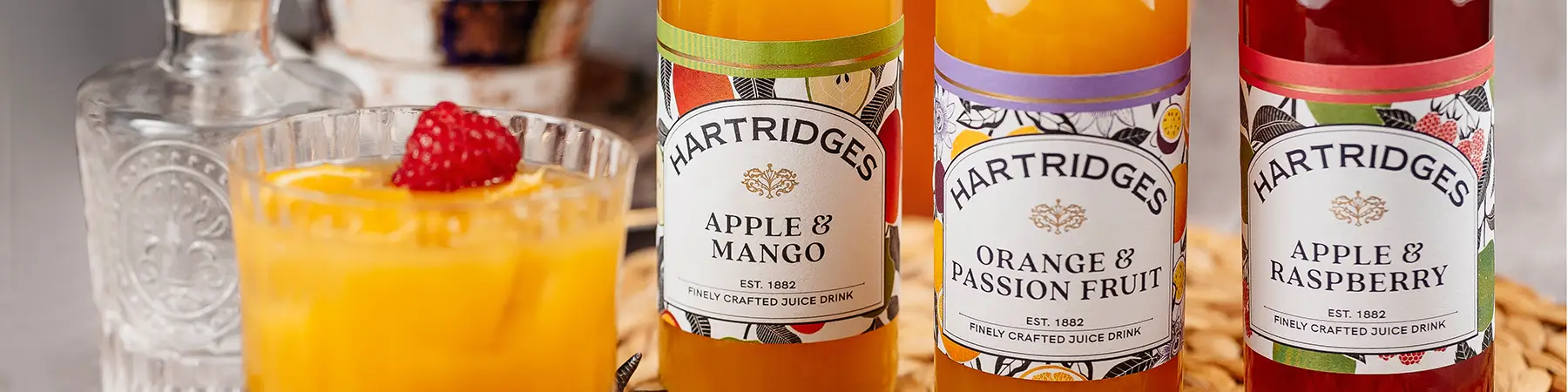 bottles of hartridges juices next to glass with raspberry in on table