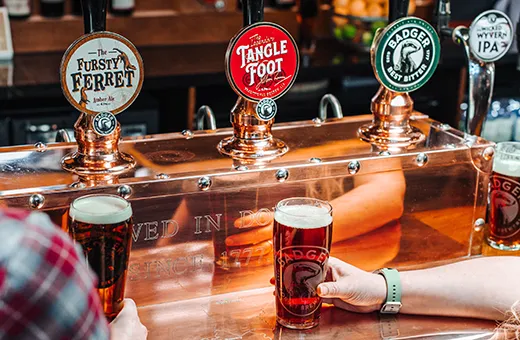 people holding pints of beers in front of beer taps